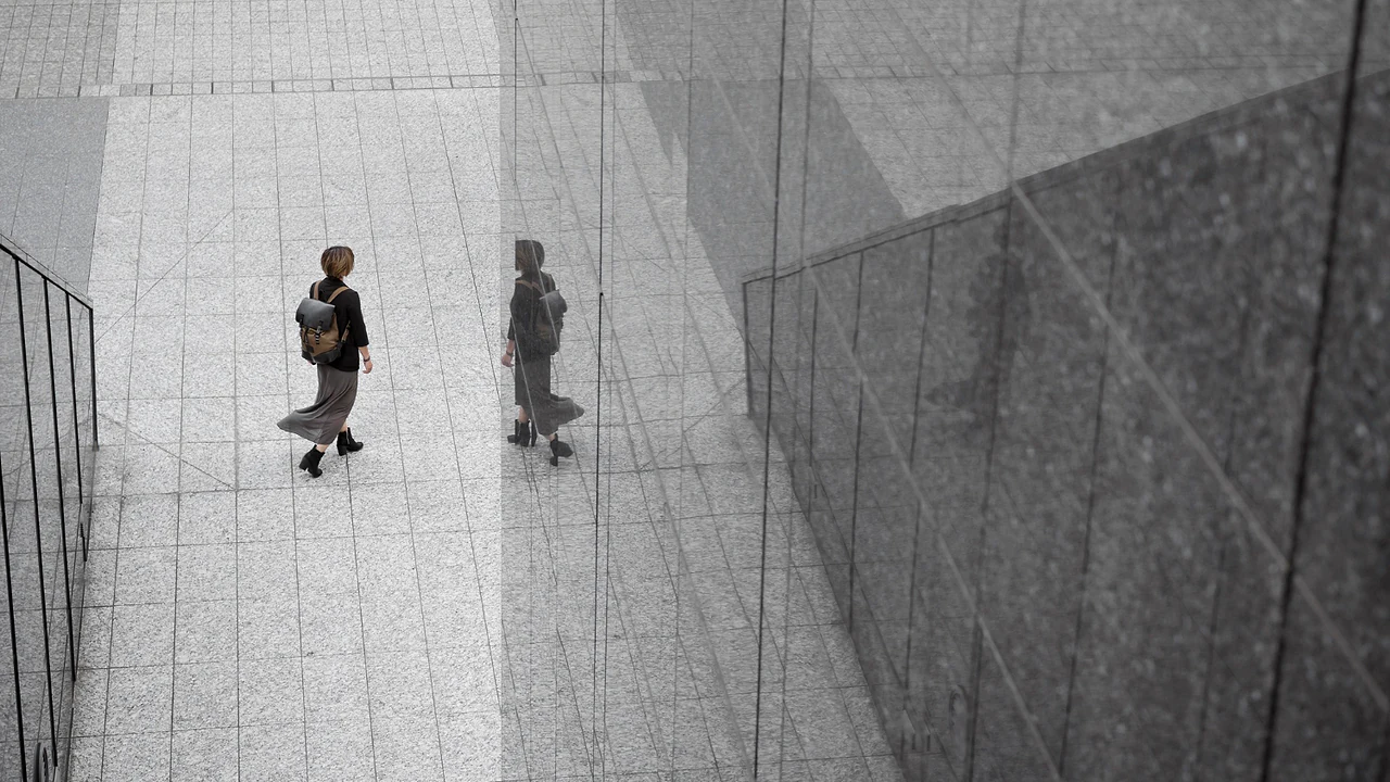 A woman walking across a stone plaza beside a reflective glass wall