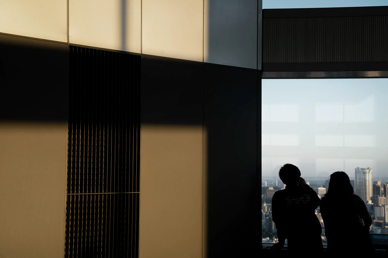 Two people silhouetted at a tall window overlooking a city