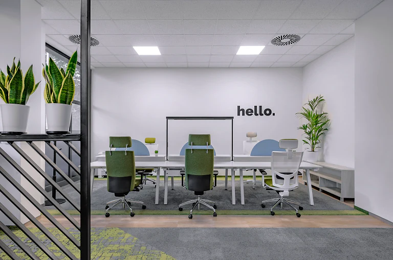 A bright co-working meeting room with green chairs and plants