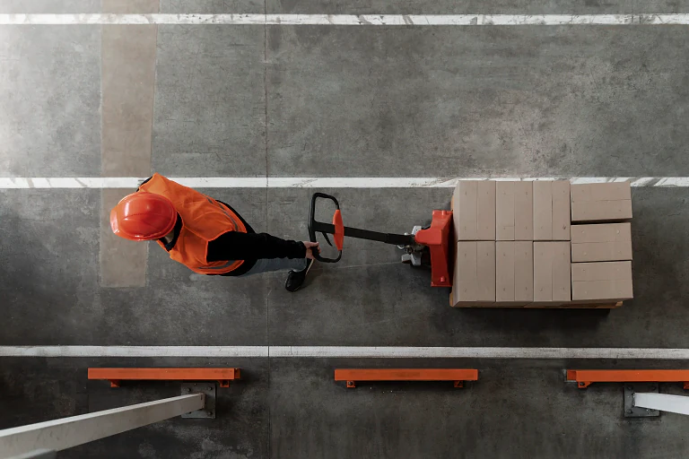 A worker pulling a pallet of boxes across a warehouse floor, seen from above