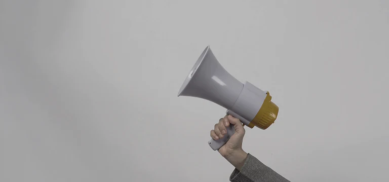 A hand holding a megaphone against a pale grey wall