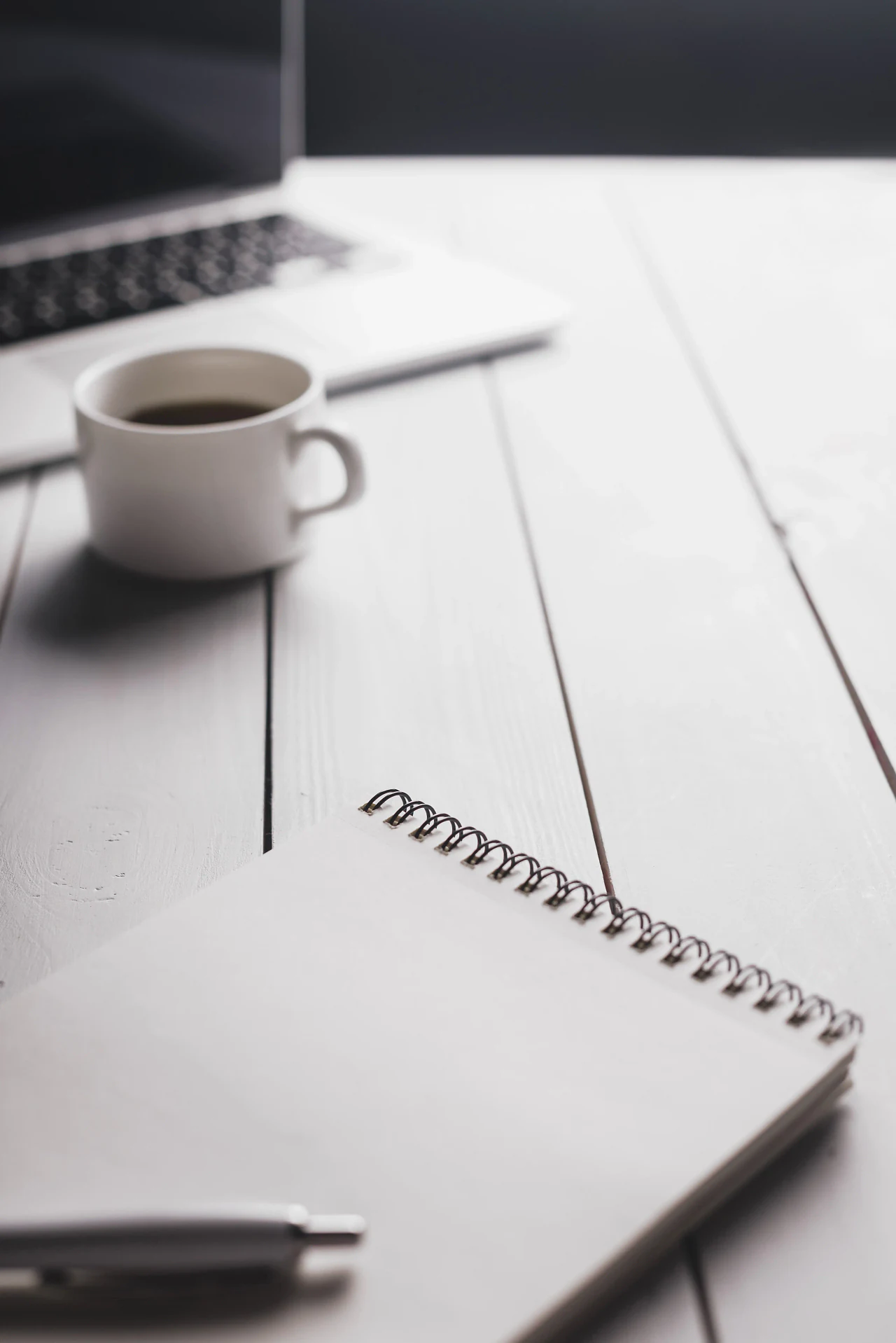 A cup of coffee and a spiral notebook on a white wooden table