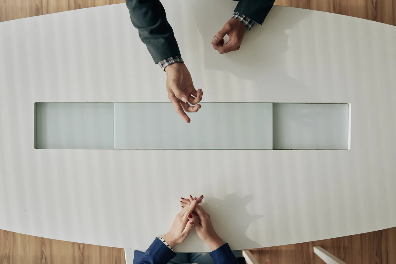 Two people facing each other across a white meeting table, seen from above
