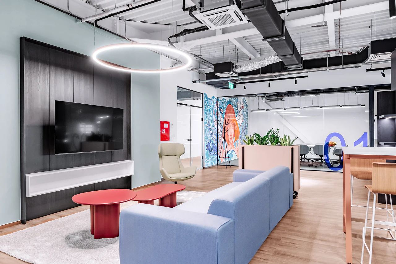 A lounge with a blue sofa, red tables and a wall-mounted screen