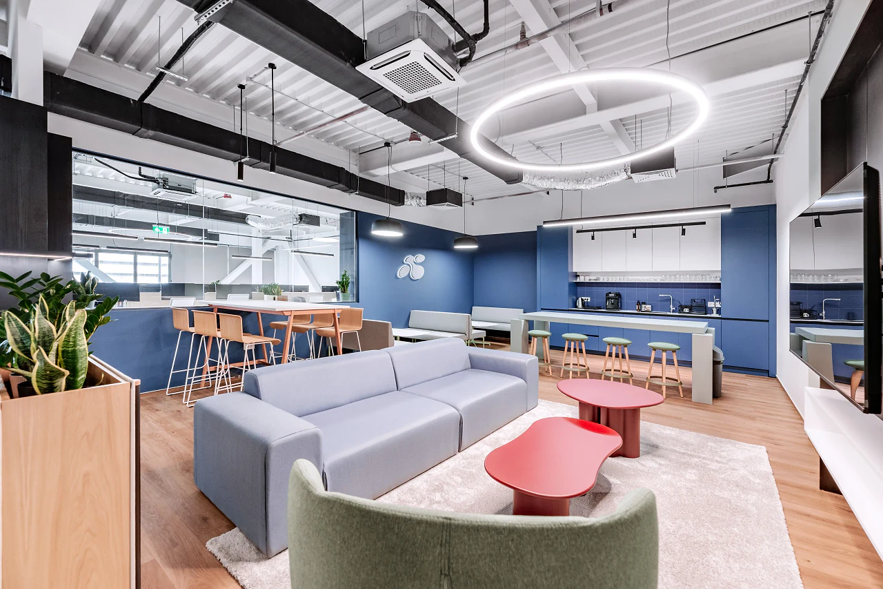 A lounge with blue sofas and red tables under a ring light