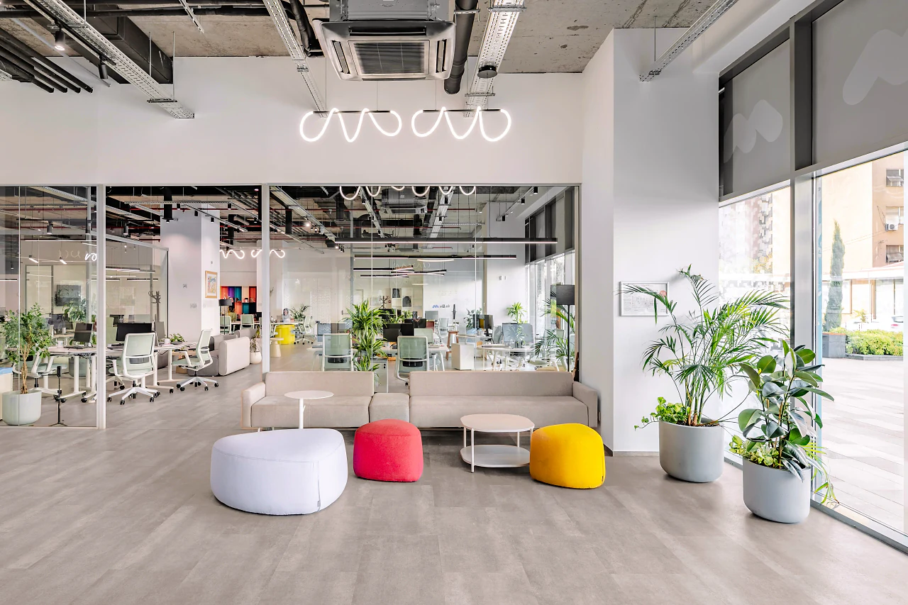 A lounge with white, red and yellow poufs among plants, desks beyond