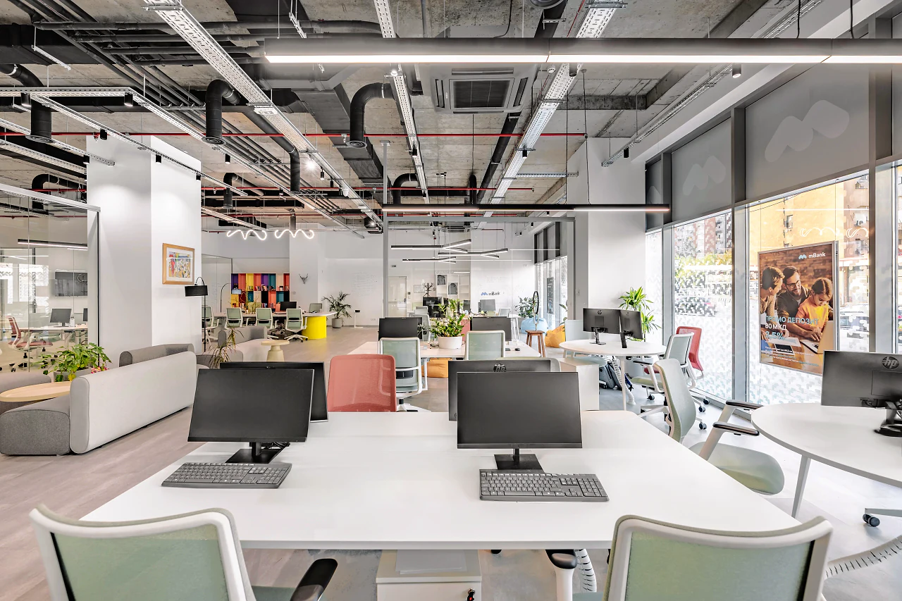 Paired desks with monitors and pale green chairs under exposed ductwork