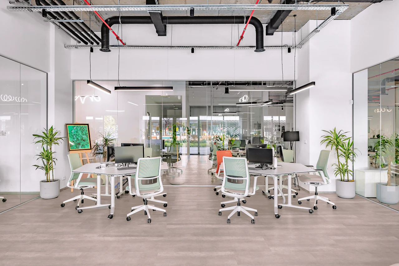 The open-plan floor, desk clusters and planting under red services