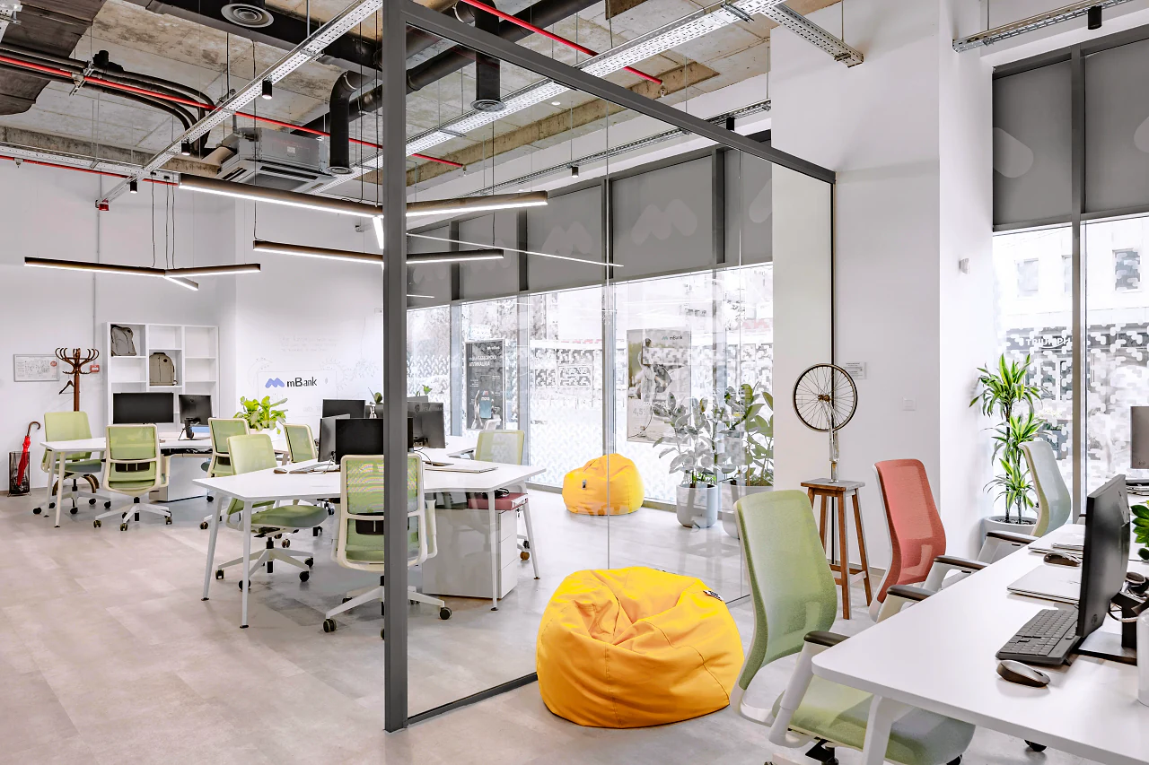 A glass meeting room with a yellow beanbag, open desks around it
