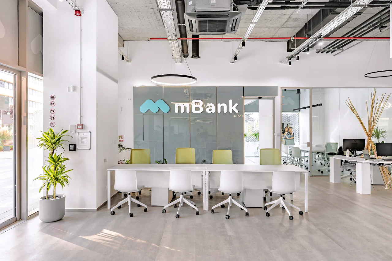 The mBank name on a slate wall behind a row of white desks and pale green chairs