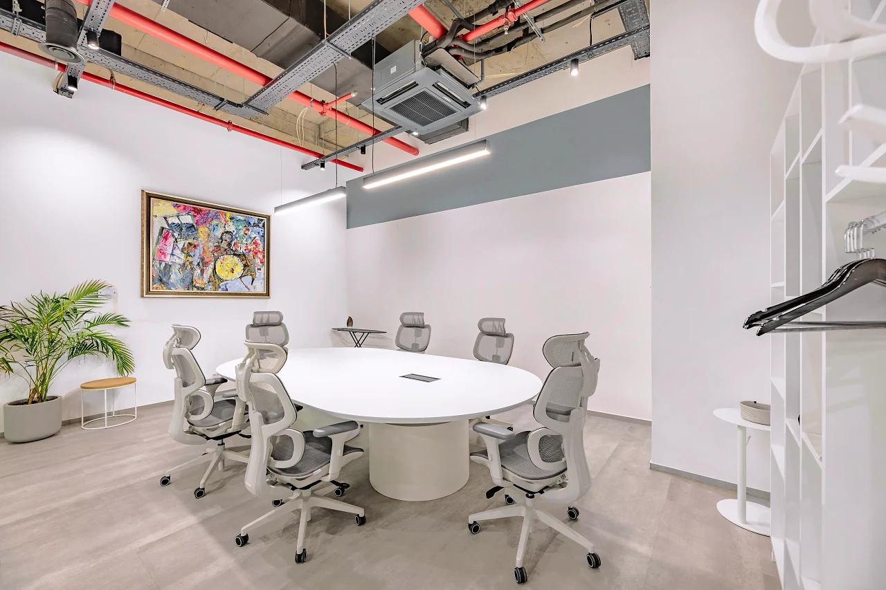 A round white meeting table and grey chairs under a colourful painting