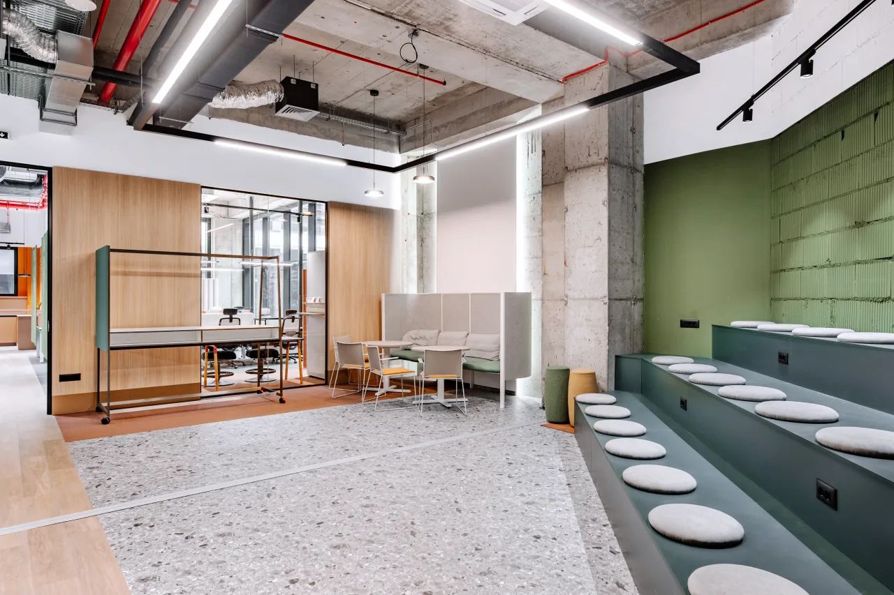 The open co-working floor with stepped green seating and a terrazzo floor