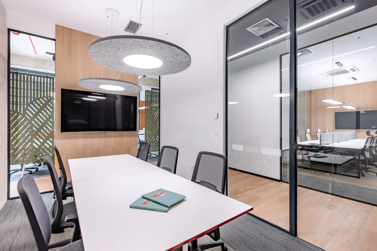 A meeting room with a white table, a round acoustic light and glass walls
