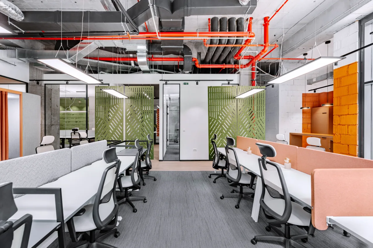 Rows of desks with pink screens under exposed red pipes