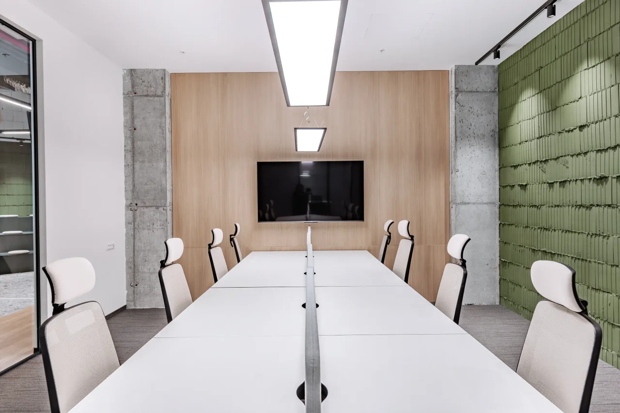 A long meeting table facing a screen beside a green acoustic wall