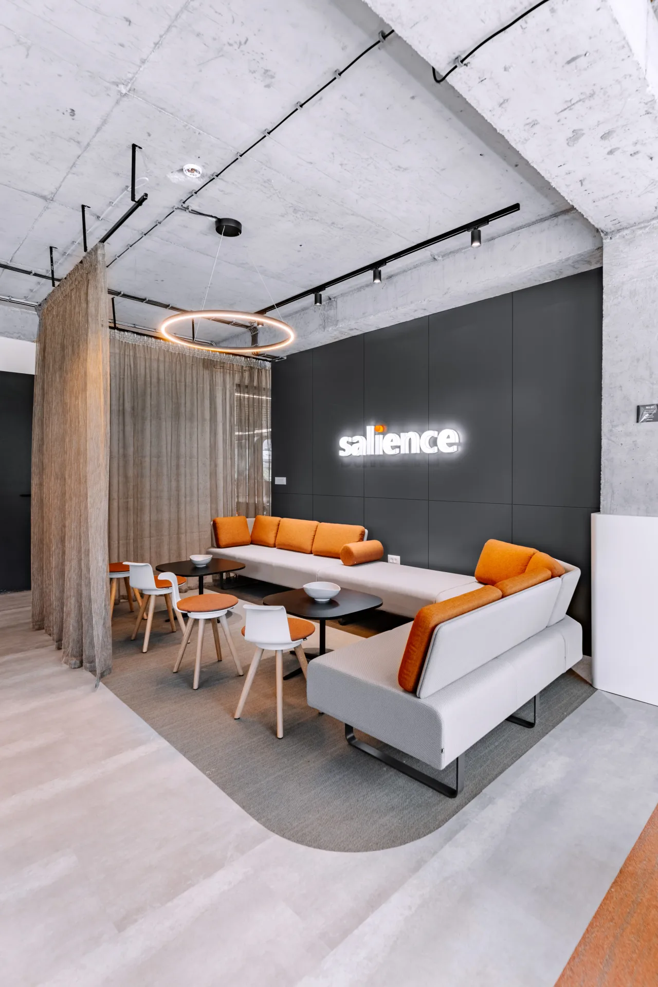 A lounge corner beside a sheer curtain and the illuminated Salience sign