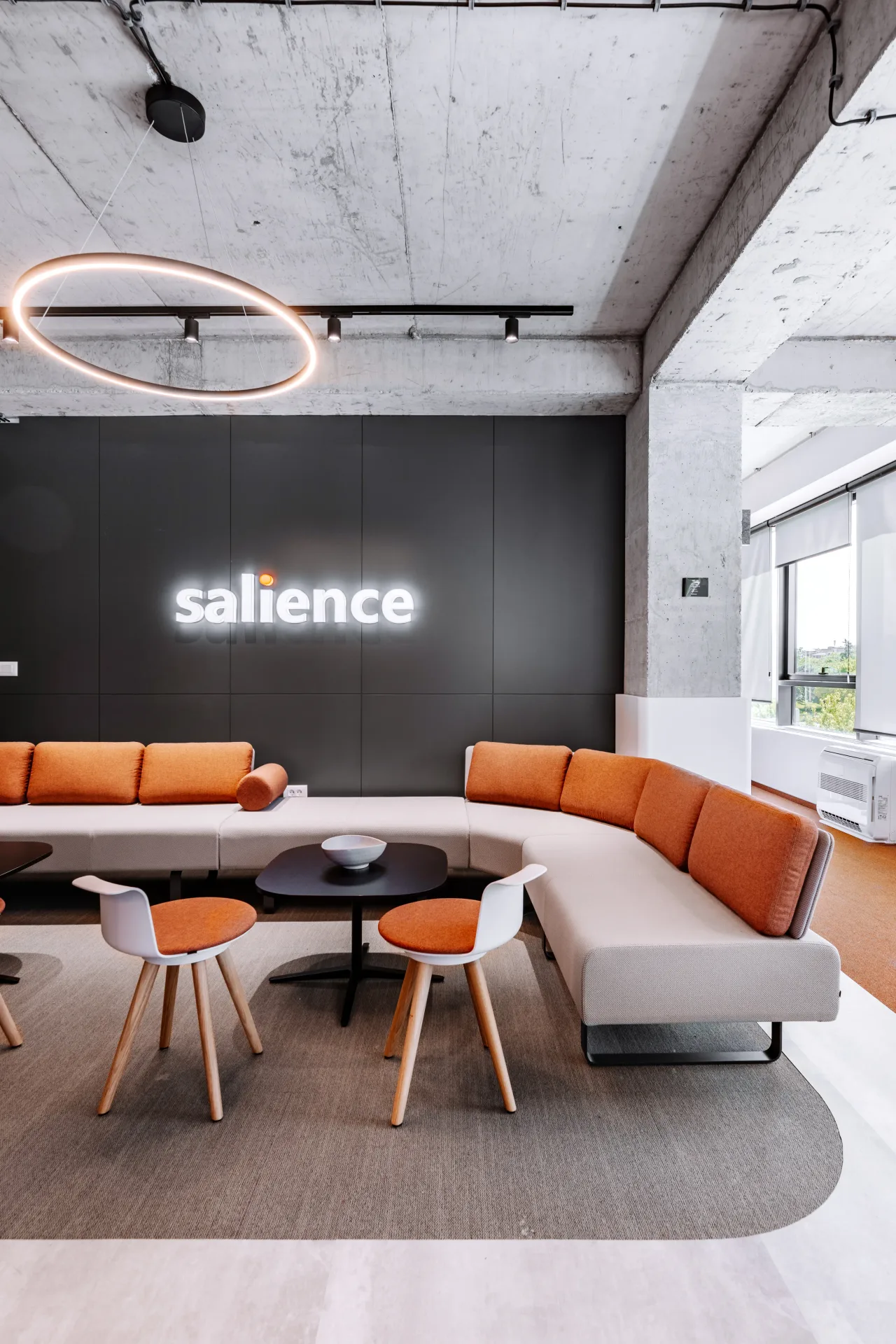 Orange chairs and a curved sofa in front of the Salience sign