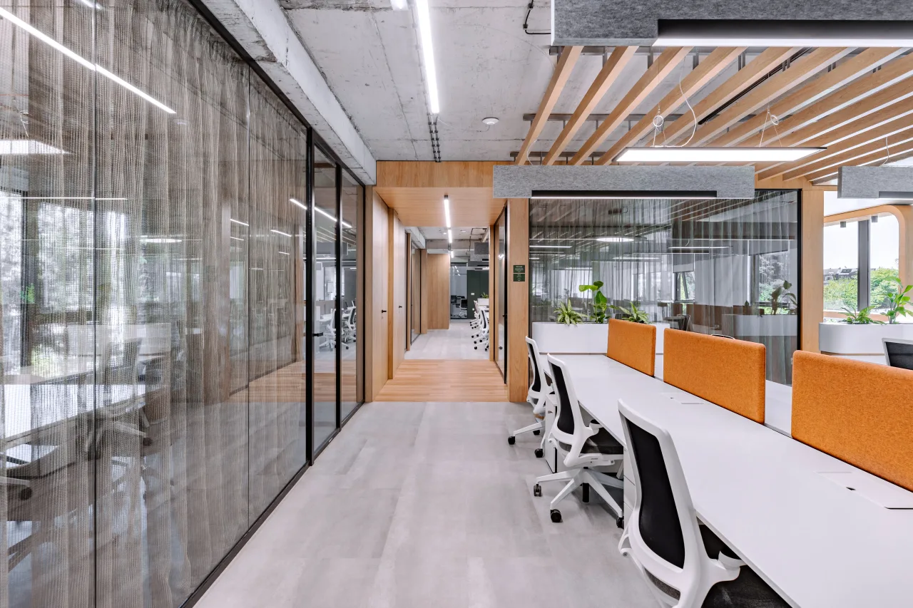 A corridor between glass meeting rooms and orange-screened desks
