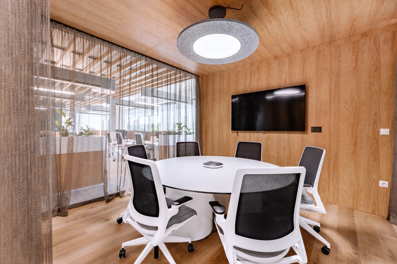 A round white meeting table in a timber-lined room with a screen