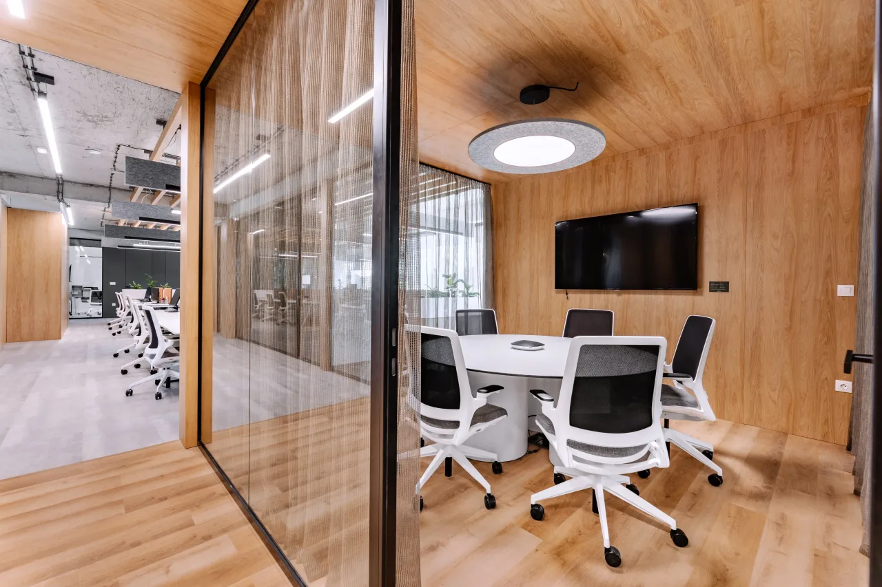 A meeting room with a round table behind glass, desks beyond
