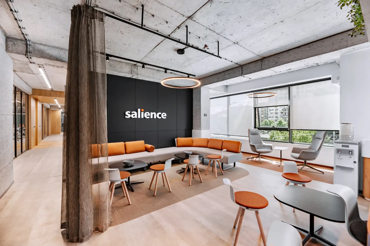 A lounge with orange sofas and stools in front of a dark wall with the illuminated Salience sign