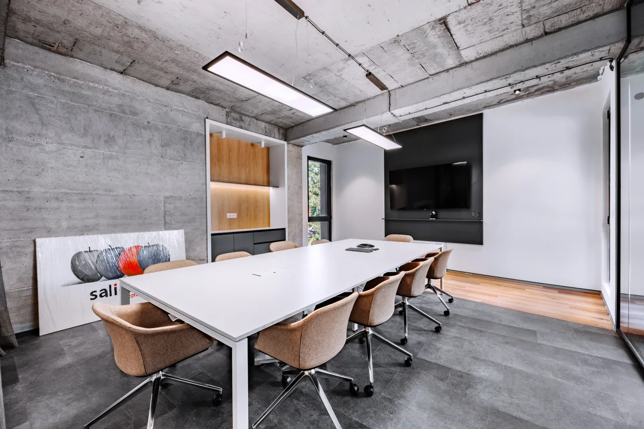A boardroom with a long white table and tan chairs under a concrete ceiling