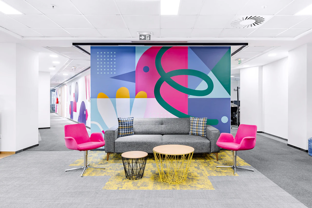 A lounge with pink armchairs and a grey sofa in front of a bold graphic wall