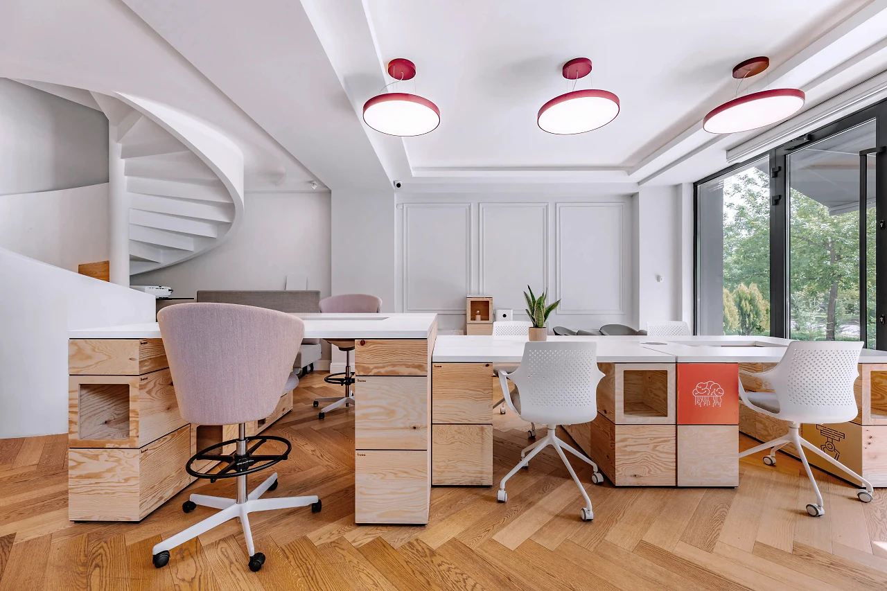A bright co-working office with wooden desks, pink chairs and a spiral staircase