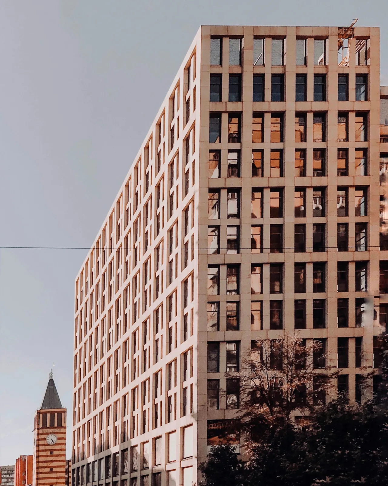 A tall office building with a warm stone grid facade against a pale sky