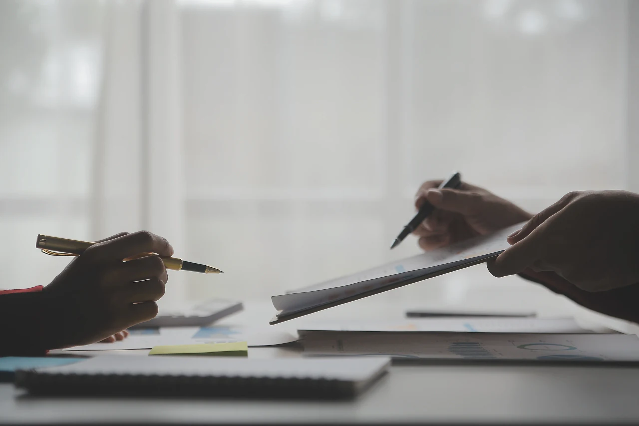 Two people reviewing documents with pens at a bright desk